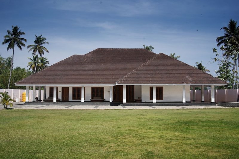 A single-storey bungalow with a wide veranda under palm trees.