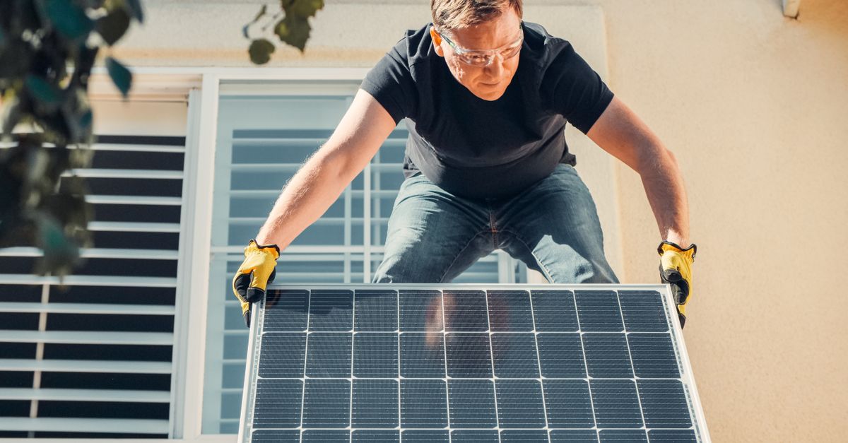 An installer wearing safety glasses and work gloves fitting a solar panel onto a rooftop mounting rail
