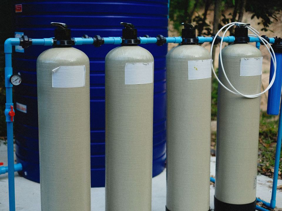 Four beige tanks in an outdoor water treatment setup with blue piping.